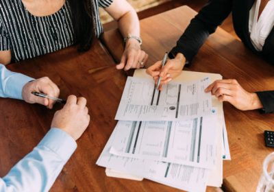 A female financial advisor and accountant meets with a married couple in their home to discuss investments and income. They are sitting at a table discussing savings, investments and taxes. Image taken in Utah, USA.